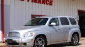 Silver Chevrolet SUV parked in front of a white building with a red 'WE FINANCE' sign above the entrance, captured on a sunny day.