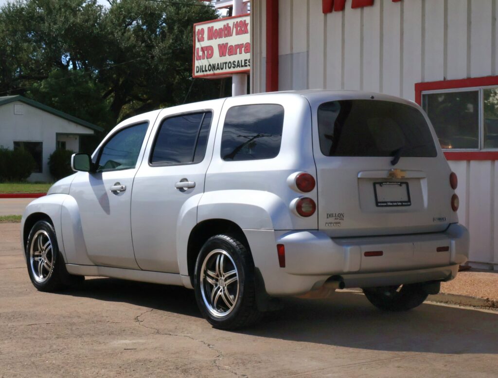 Silver Chevrolet SUV parked in a lot beside a white building with red trim and a Dillon Auto Sales sign in the background.