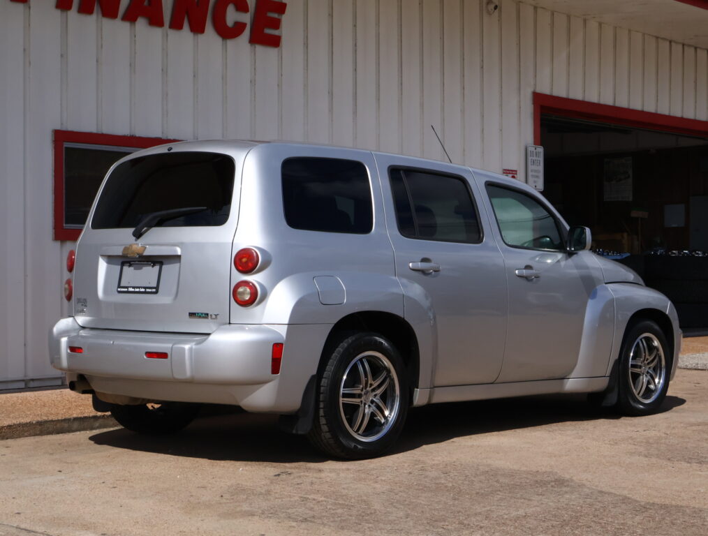 Rear and side view of a silver Chevrolet SUV parked in front of a white building with red trim. The windows are tinted and the tail lights are visible.]