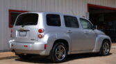 Rear and side view of a silver Chevrolet SUV parked in front of a white building with red trim. The windows are tinted and the tail lights are visible.]