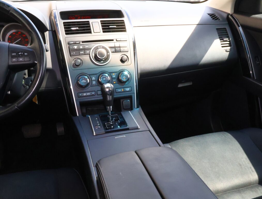 Interior of a car focusing on the center console with climate controls and radio knob cluster and gear lever nearby.
