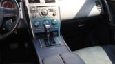 Interior of a car focusing on the center console with climate controls and radio knob cluster and gear lever nearby.