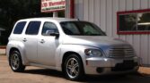 Silver Chevrolet SUV parked in front of a beige building with red trim and tinted windows.