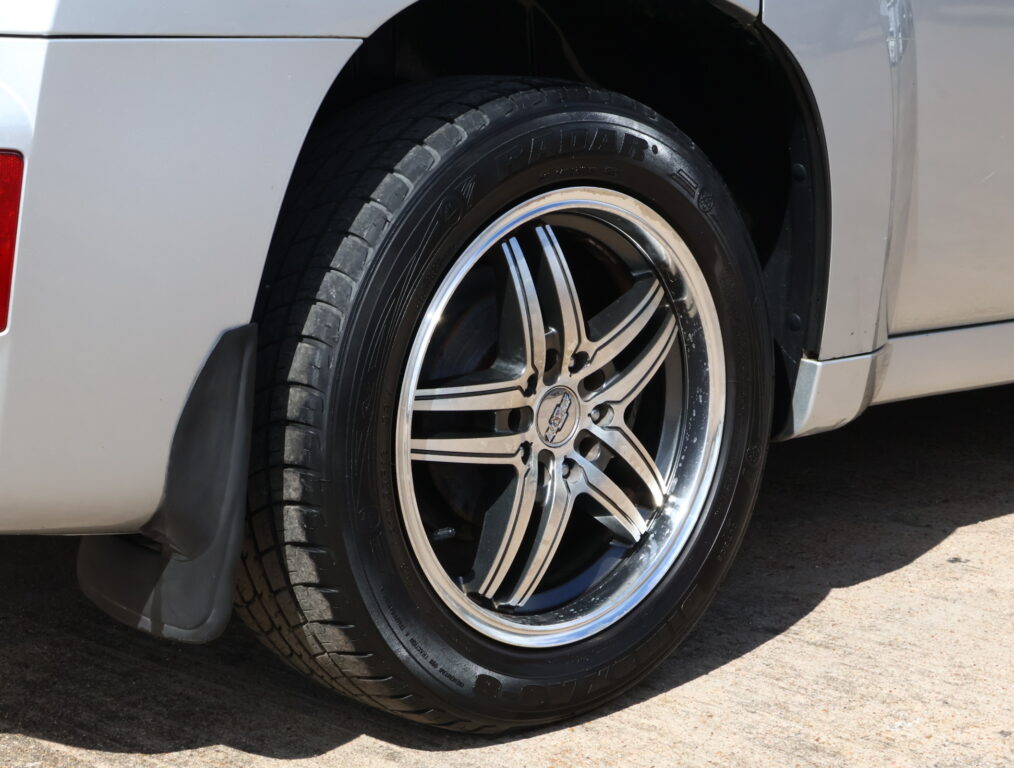 Close-up of a car wheel with an alloy rim and black tire against a silver vehicle panel, visible tire tread and rim details.