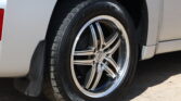Close-up of a car wheel with an alloy rim and black tire against a silver vehicle panel, visible tire tread and rim details.