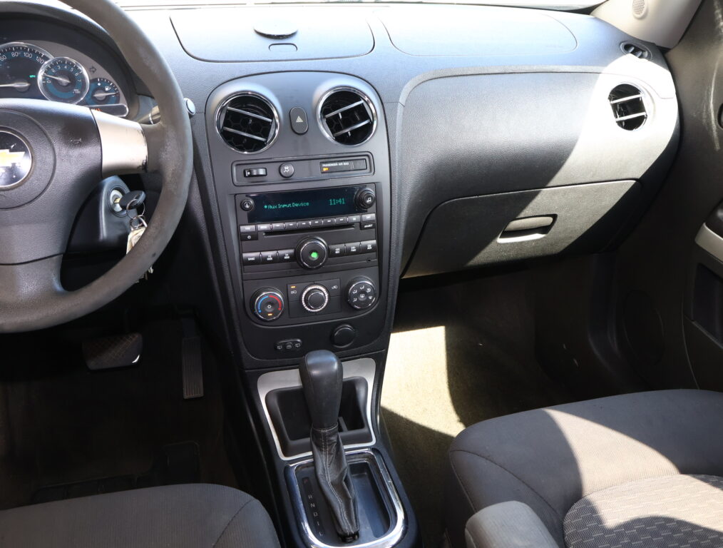 Interior of a car showing the steering wheel on the left and a center console with two round air vents, hazard button, and radio beneath it.