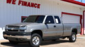 Silver pickup truck parked in front of a white building with red trim and a large 'WE FINANCE' sign on the wall