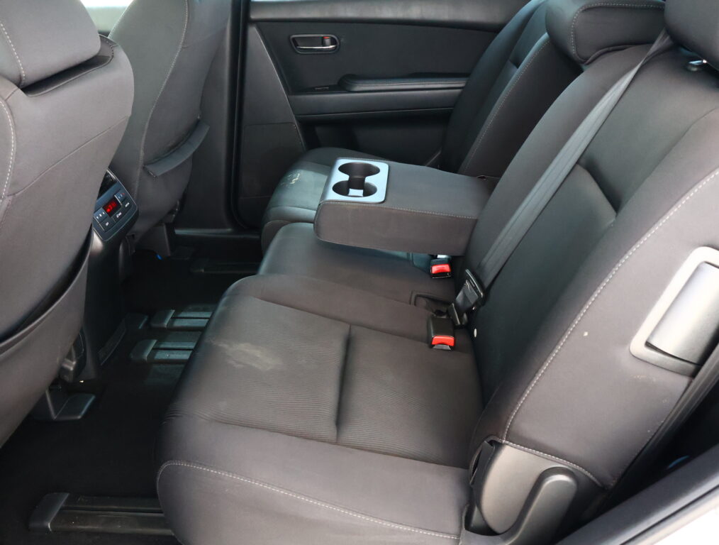 Rear car seats with a fold-down center armrest housing two cupholders and black upholstery.