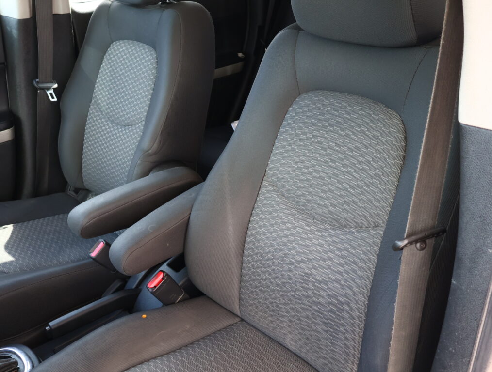 Front car seats with gray patterned fabric and visible seat belts; center console between seats partially visible.