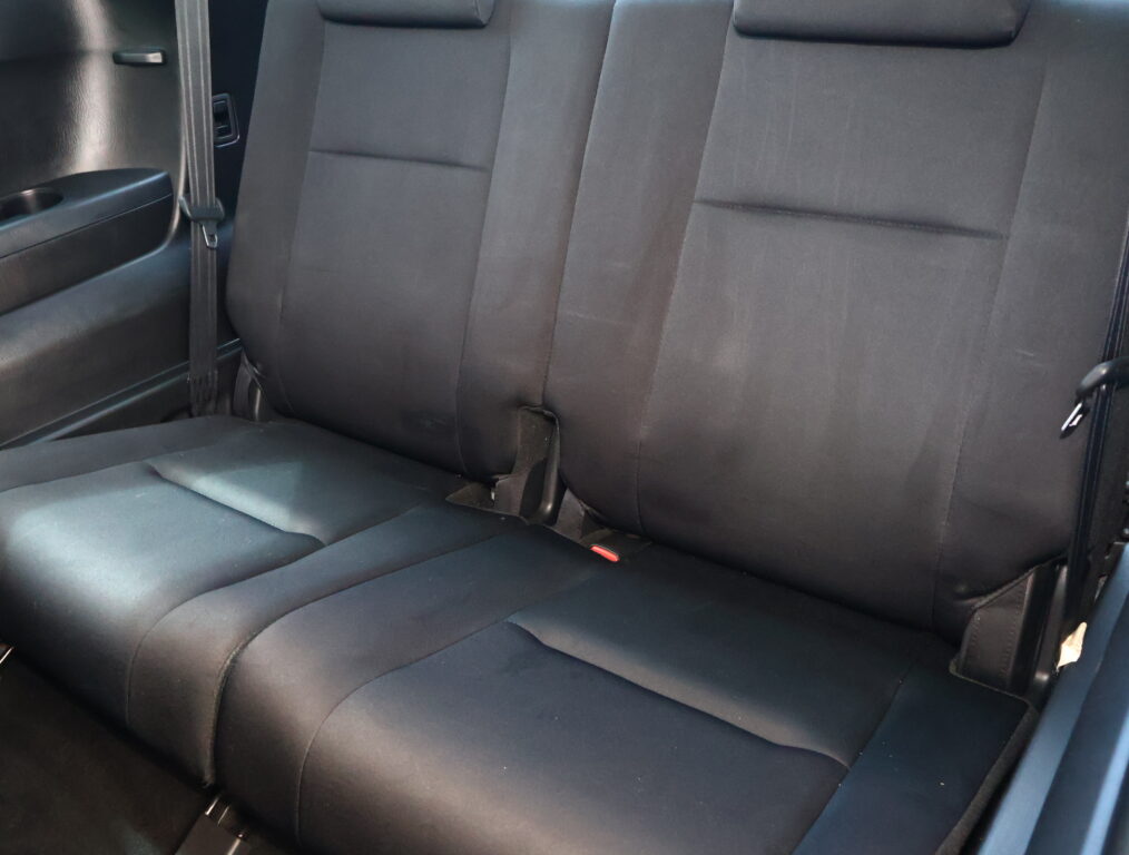 Back seat of a dark gray car with three-seat bench, visible seat belts and headrests, interior door panel nearby.