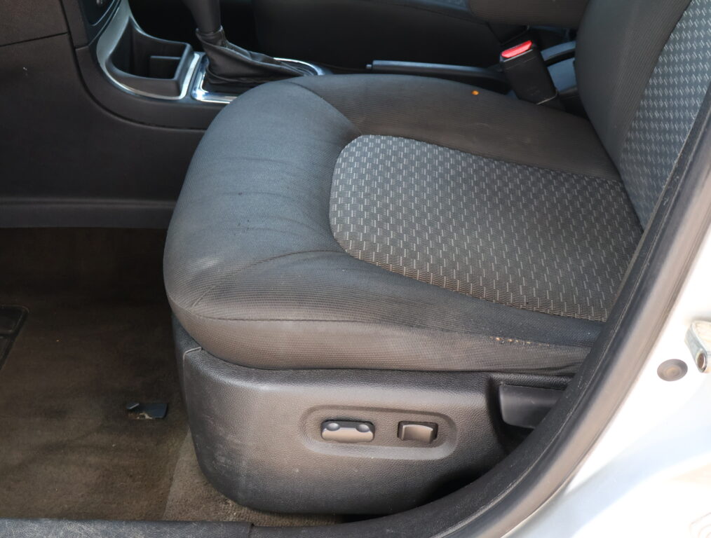 Inside a car cabin showing the front seat with black patterned fabric, center console, gear shifter, and seat adjustment controls at the side
