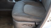 Inside a car cabin showing the front seat with black patterned fabric, center console, gear shifter, and seat adjustment controls at the side