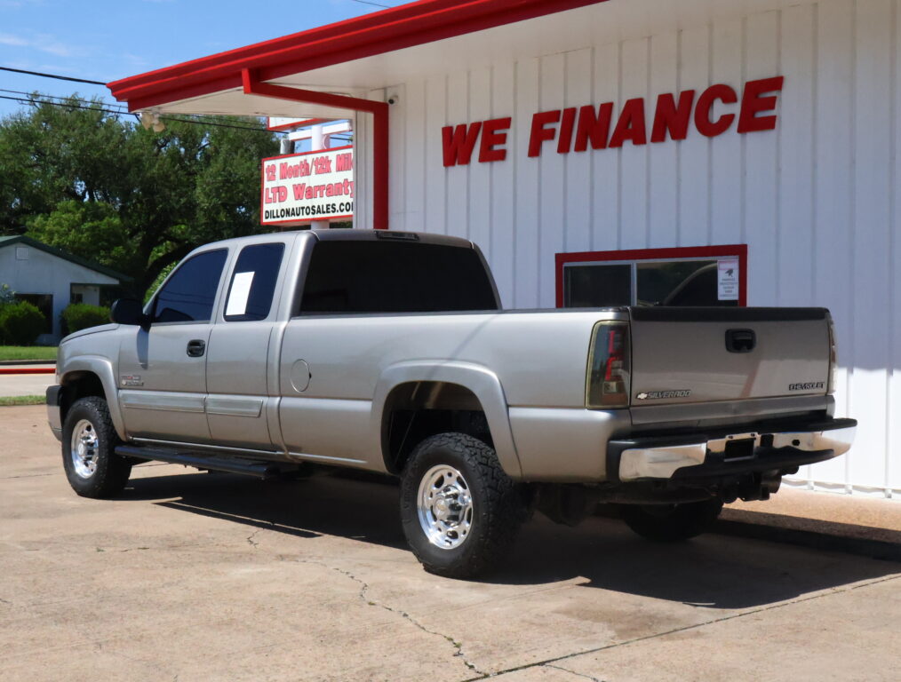 Silver Chevrolet Silverado pickup truck parked in front of a white building with red trim and a 'We Finance' sign.