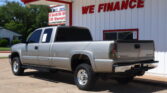 Silver Chevrolet Silverado pickup truck parked in front of a white building with red trim and a 'We Finance' sign.