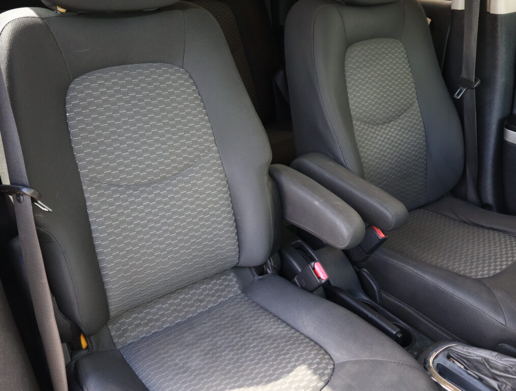 Interior of a car showing two front seats with gray patterned upholstery and visible seat belts.