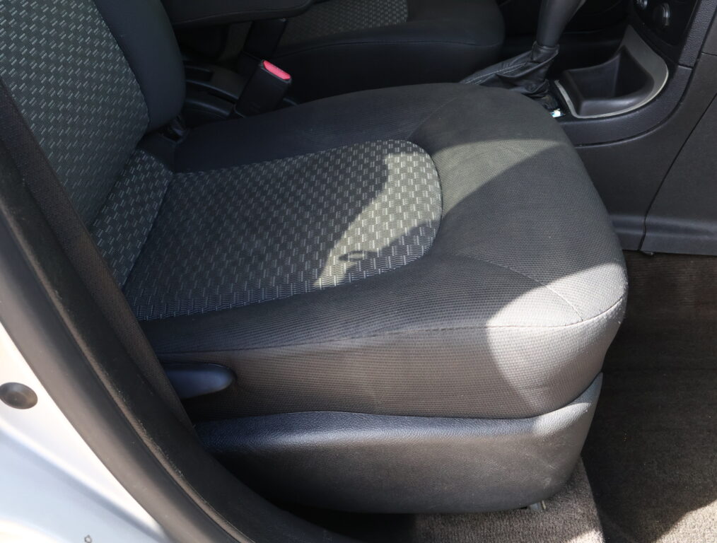 Front passenger seat and center area of a car interior, showing dark fabric upholstery and a red seat belt buckle nearby