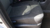 Front passenger seat and center area of a car interior, showing dark fabric upholstery and a red seat belt buckle nearby