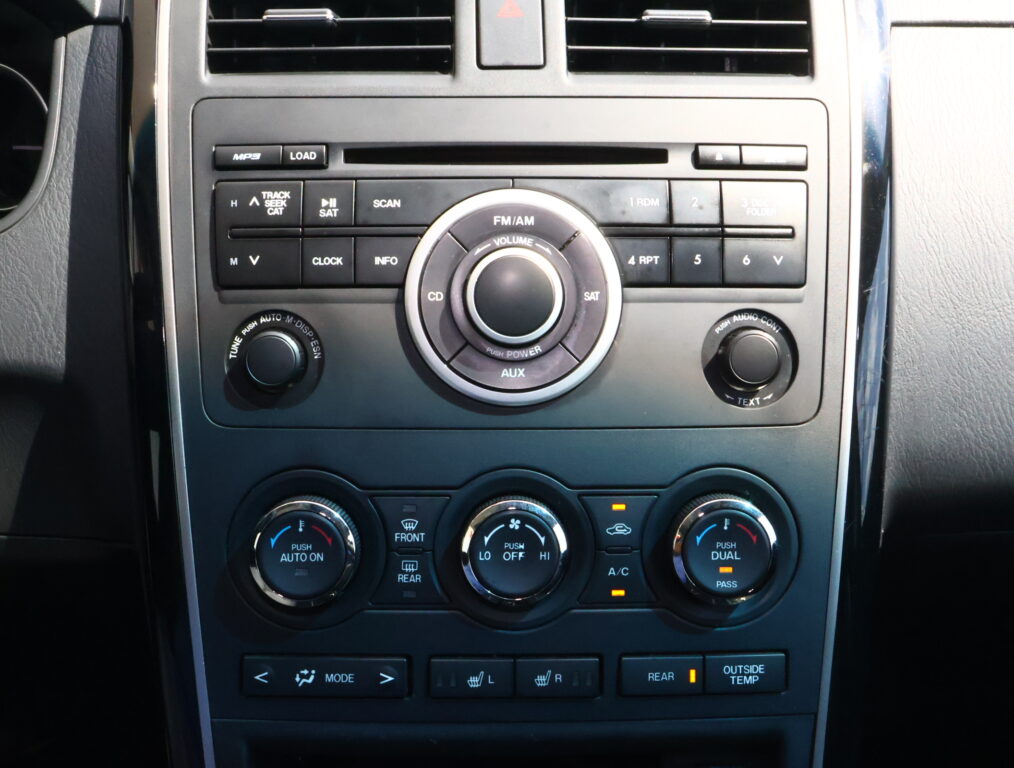Center console of a car with a radio and climate controls: circular volume knob surrounded by buttons and preset keys on the dashboard.