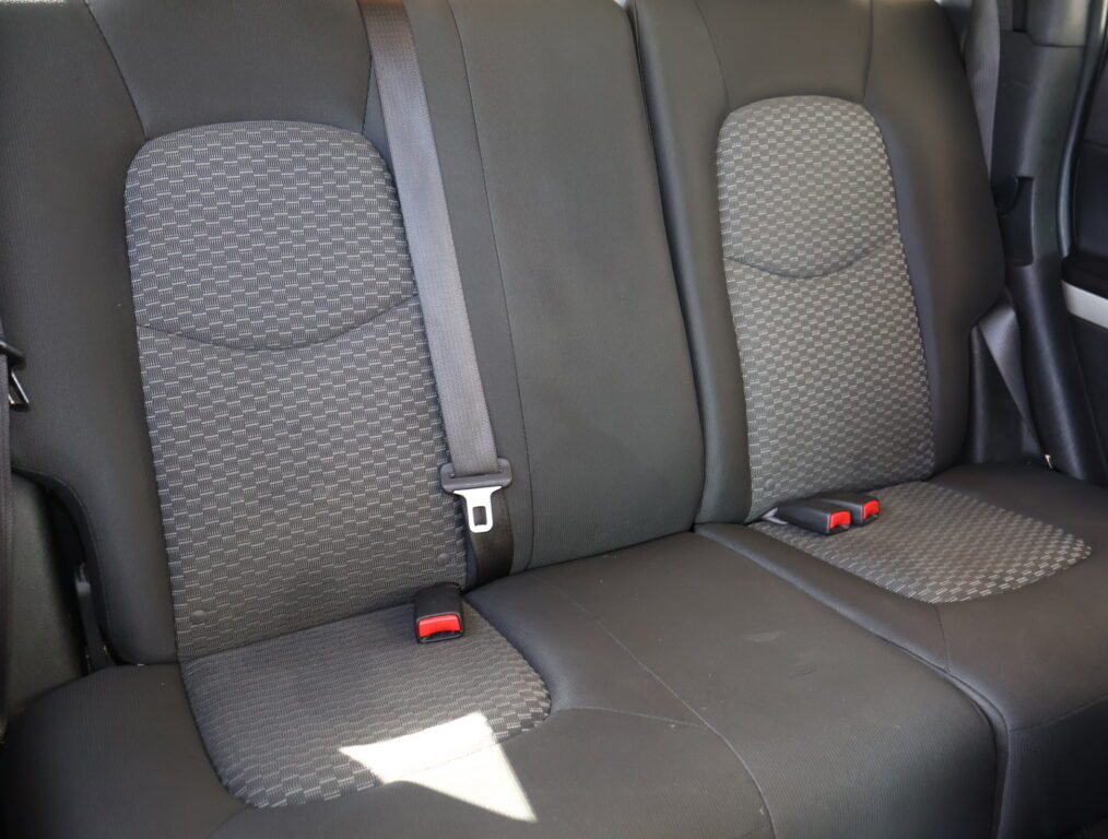 Back seat of a car with two patterned fabric cushions and visible seat belts, including red buckle tips on either side.