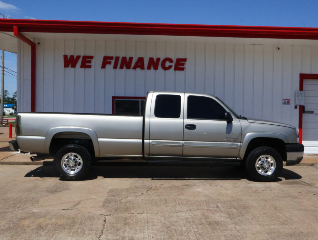 Silver pickup truck parked in front of a white building with a large red 'WE FINANCE' sign under a blue sky.