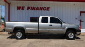 Silver pickup truck parked in front of a white building with a large red 'WE FINANCE' sign under a blue sky.