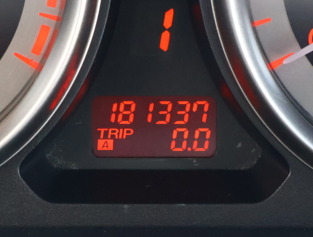 Close-up of a car dashboard digital display showing trip meters in red, with the numbers partially visible (0.00) and surrounding red indicators.