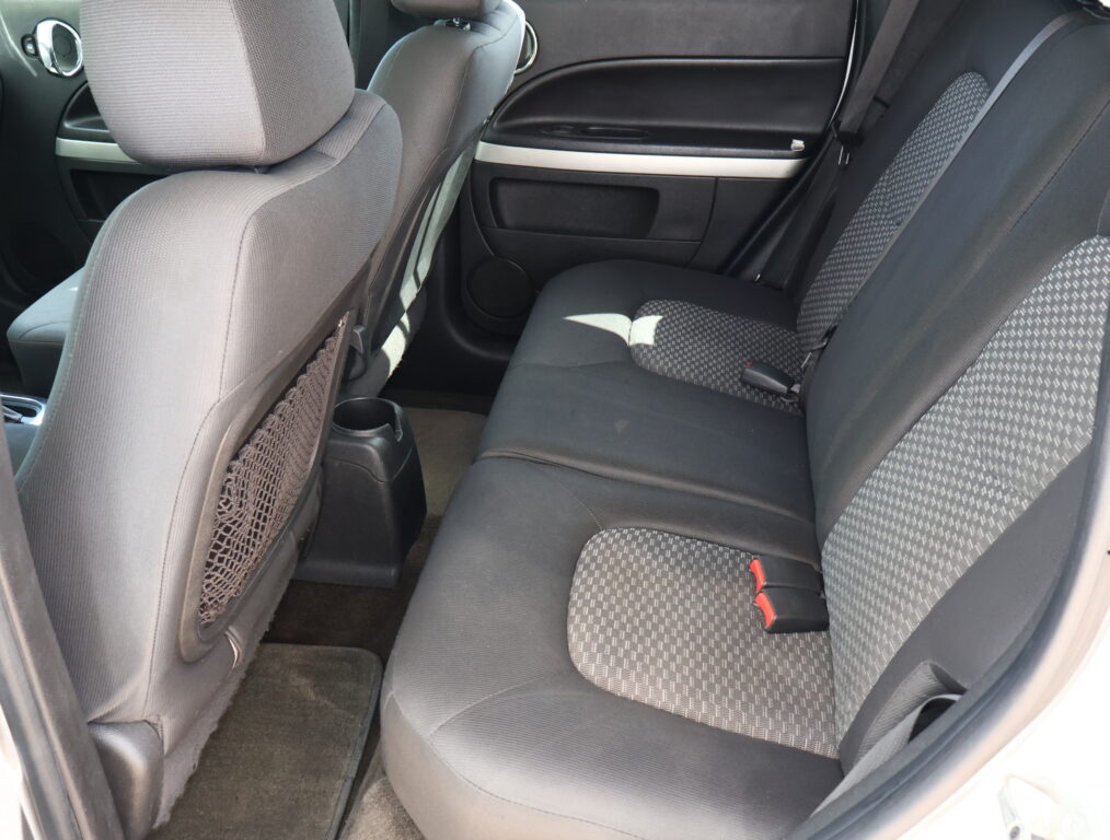Rear seating area of a car with gray fabric upholstery, visible seatbelts, and door panel in the background as the photo is taken from the side door.