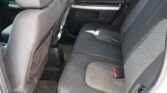 Rear seating area of a car with gray fabric upholstery, visible seatbelts, and door panel in the background as the photo is taken from the side door.