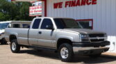 White pickup truck parked in front of a white building with red trim and a large 'WE FINANCE' sign behind.