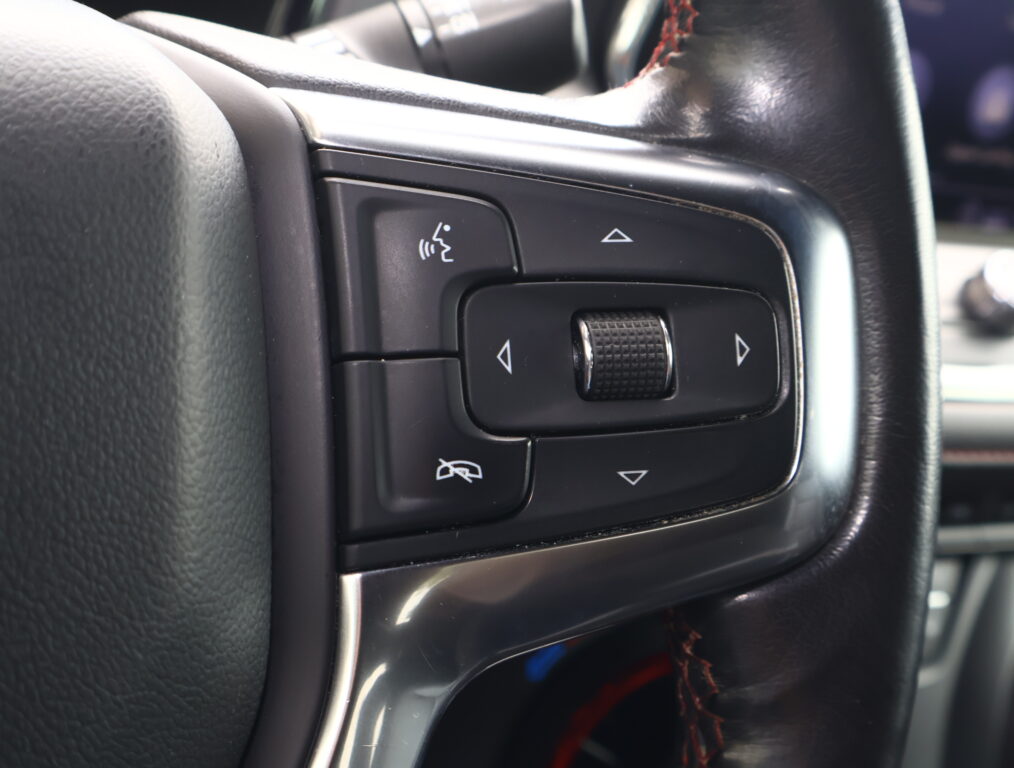 Close-up of a car steering wheel control panel with a textured roller and directional arrows on black plastic surface.