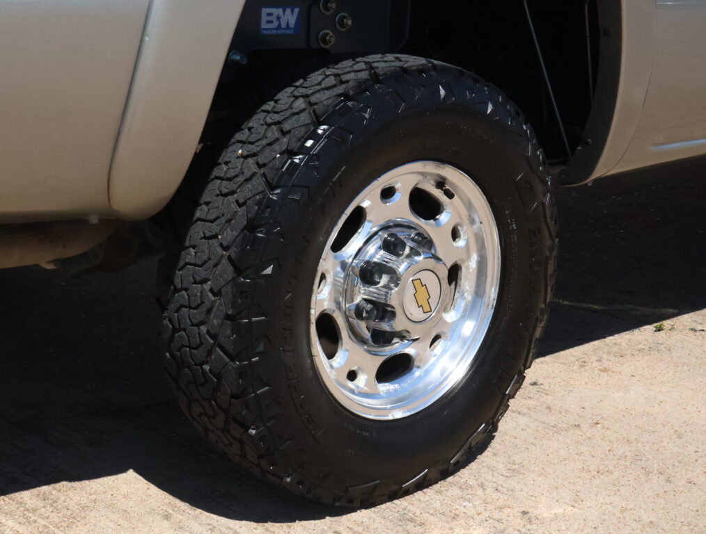 Close-up of a rugged off-road tire mounted on a chrome wheel beside a beige vehicle body.