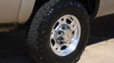 Close-up of a rugged off-road tire mounted on a chrome wheel beside a beige vehicle body.
