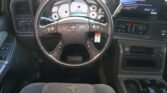 Driver's seat view of a pickup interior: steering wheel, analog gauge cluster, and a large infotainment touchscreen to the right.