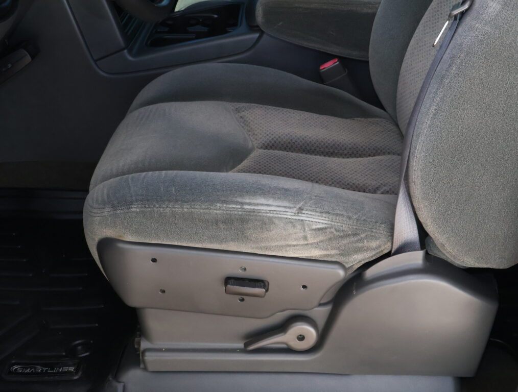 Front passenger seat in a dark gray car interior with visible seat adjustment lever and red seat belt buckle nearby.