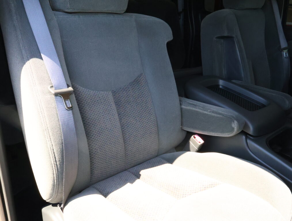 Gray cloth car seats with visible seat belts and a center armrest, showing interior of a vehicle.