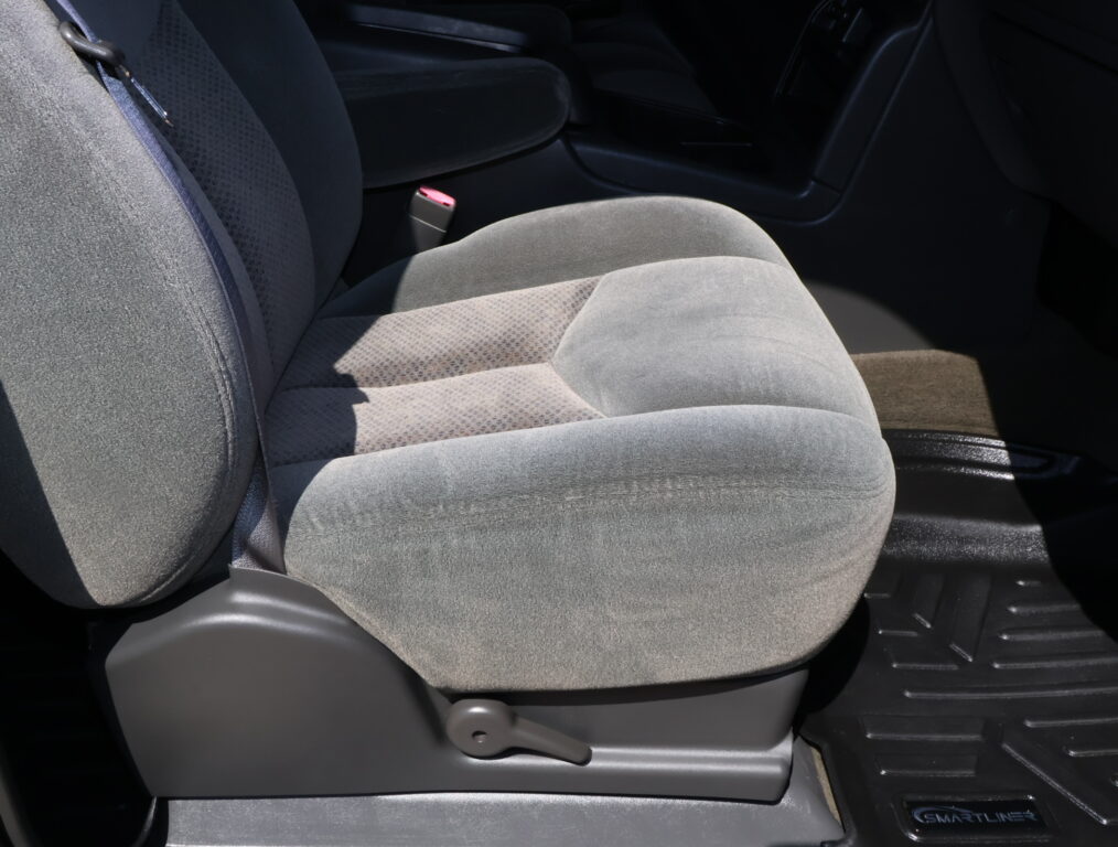 Gray cloth car seat with a red seatbelt buckle between the seat and center console in a vehicle interior.