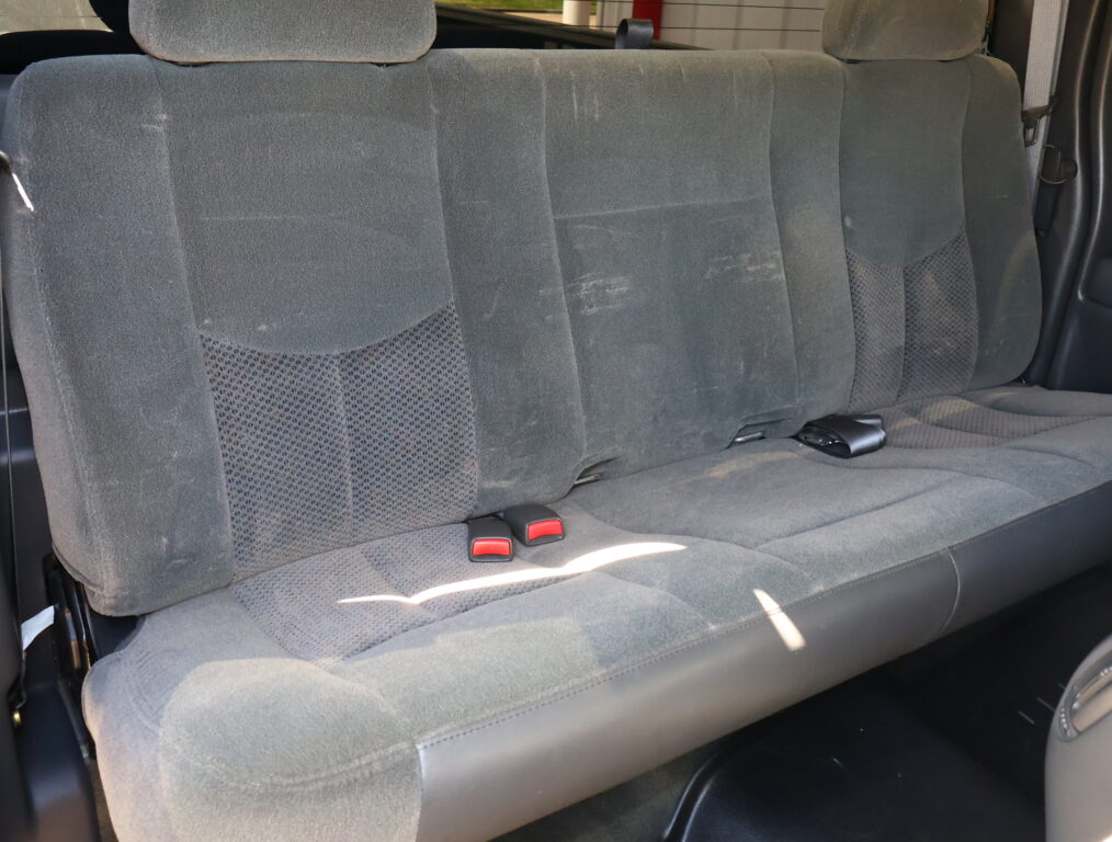 Rear car bench seat with gray fabric upholstery, three seating sections, and visible red seat belt buckles.