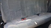 Rear car bench seat with gray fabric upholstery, three seating sections, and visible red seat belt buckles.