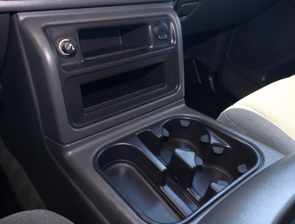 Center console of a car showing cup holders, a small storage pocket, and a 12V power outlet next to a front seat area