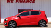 Red car parked in front of a white building with a large red 'WE FINANCE' sign on the wall behind it.