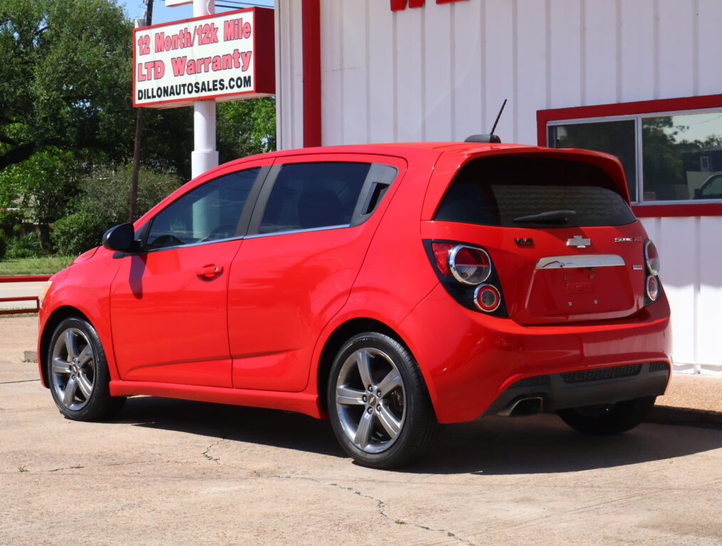 Red Chevrolet hatchback parked in front of a white building with red trim and a bright sign in the background reading 'DILLONAUTOSALES.COM'