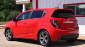 Red Chevrolet hatchback parked in front of a white building with red trim and a bright sign in the background reading 'DILLONAUTOSALES.COM'