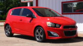 Bright red late-model SUV parked in front of a white building with red trim and a dealership signlees.