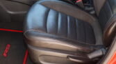 Close-up of a black leather car seat with red contrast stitching and a center console with a gear shifter visible.