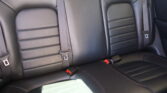 Back seat of a car with black leather upholstery and three seat belts visible, one buckled.