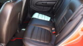 Rear car seat area with black leather upholstery and red contrast stitching.