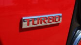 Close-up of chrome TURBO badge on a bright red car rear panel area amply lit by sunlight.