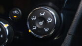 Close-up of a car climate control dial showing heated-seat icons and airflow settings, with an orange indicator light.