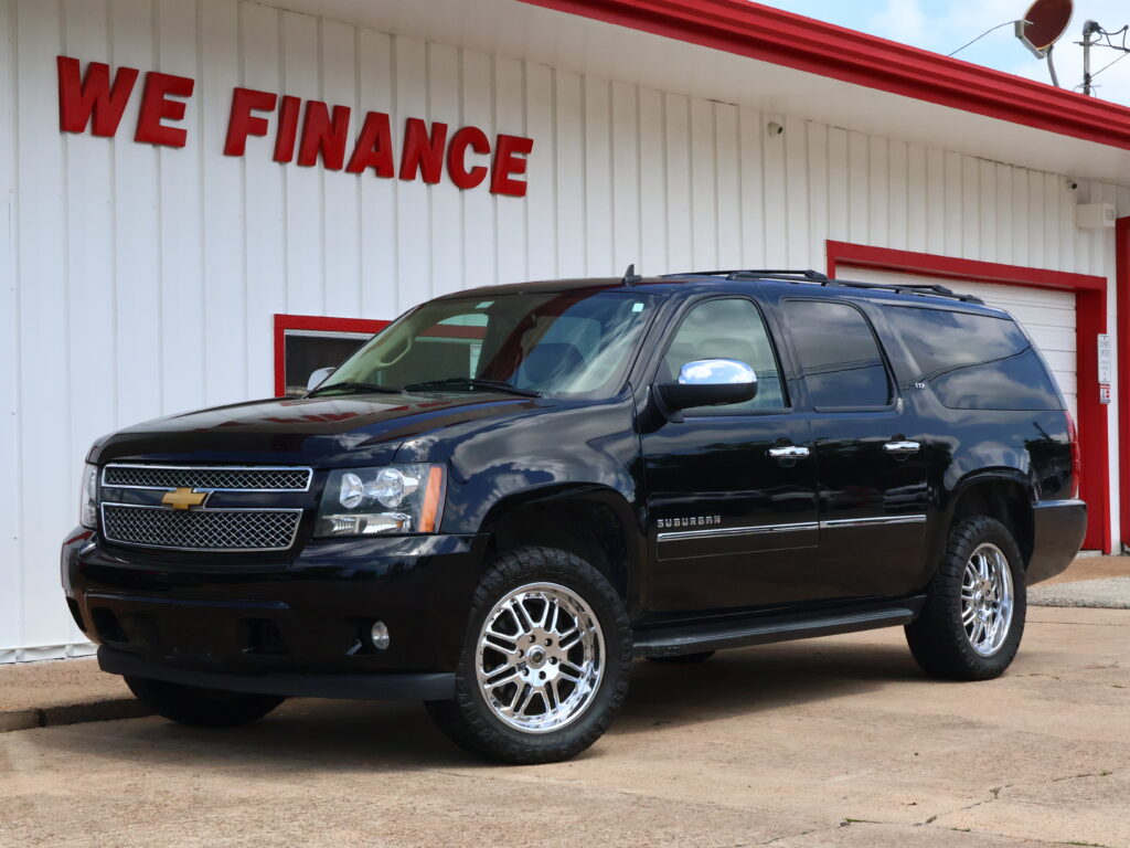 Black Chevrolet Suburban parked in front of a white building with red trim and a 'WE FINANCE' sign above.