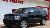 Black Chevrolet Suburban parked in front of a white building with red trim and a 'WE FINANCE' sign above.